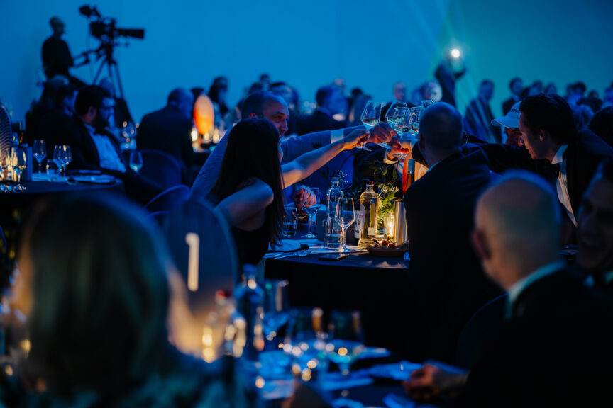 Een groep gasten aan een tafel heft hun glazen op en proost gezamenlijk tijdens het Computable Awards-evenement. ze worden omringd door een sfeervolle ambiance.