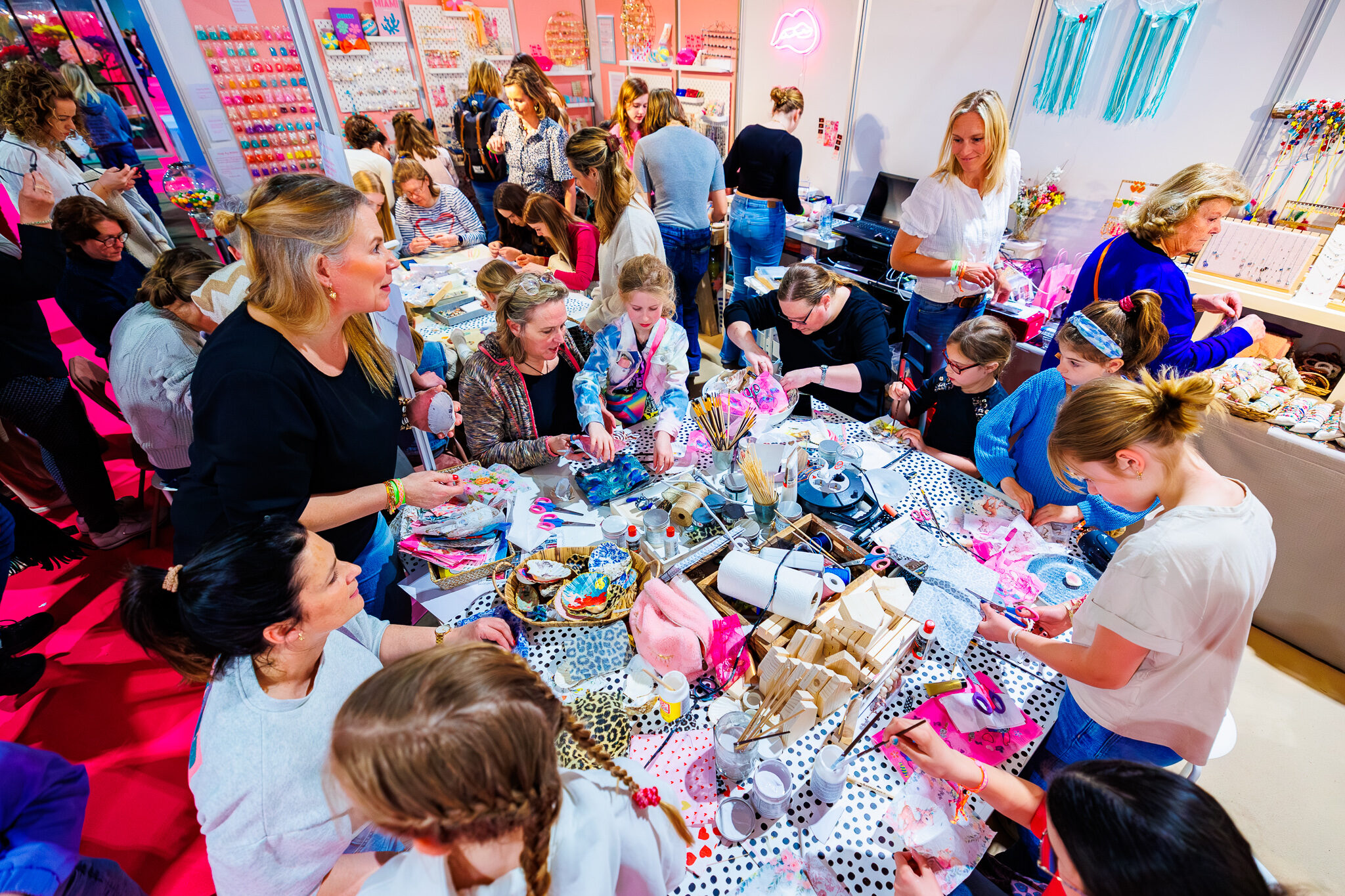Groep mensen zit om een tafel met veel knutsespullen tijdens KreaDoe.