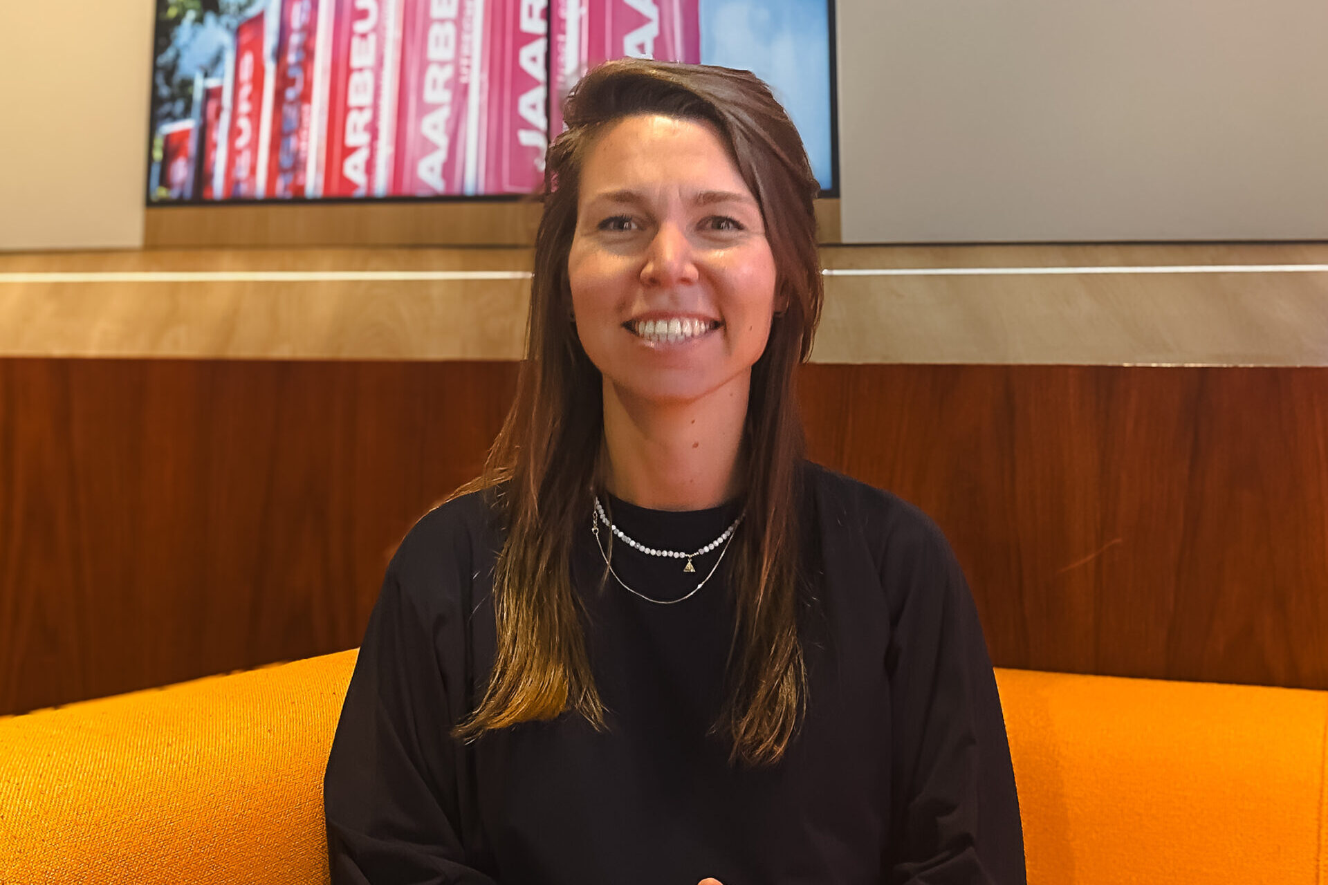 Annemijn zittend op een oranje stoel lachend naar de camera